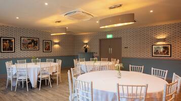 A dining area with round tables and white chairs, a wooden floor, and patterned wallpaper.