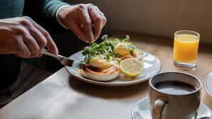 A person cutting an egg benedict dish with a lemon slice on a plate, accompanied by a glass of orange juice and a cup of coffee. - Park Head Hotel (Bishop Auckland)