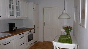 A compact kitchen with white cabinets, a wooden countertop, a coffee maker, and a dining table with a floral centerpiece. - Welcome to the harbor district - Emma (Wismar)