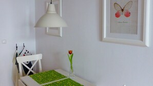 A small dining area with a white table, chairs, a green placemat, a white pendant lamp, and a framed butterfly artwork on the wall. - Welcome to the harbor district - Emma (Wismar)