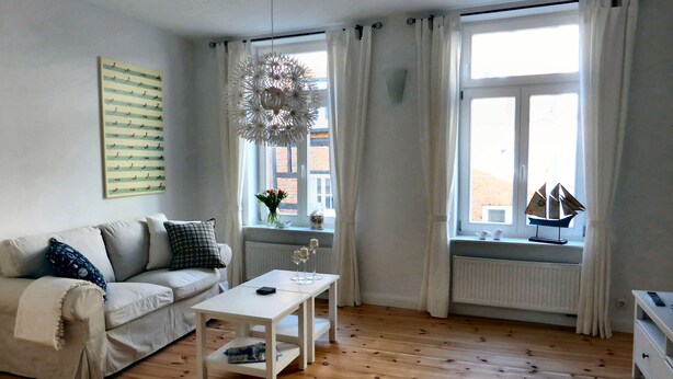 A modern living room with a sofa, a coffee table, and a window with curtains. - Welcome to the harbor district - Emma (Wismar)
