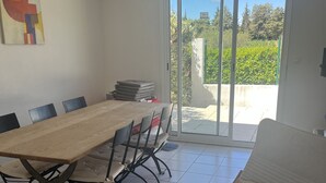 Un comedor con una larga mesa de madera y sillas, una silla moderna con cojín, y vistas a un área exterior con vegetación a través de un ventanal.