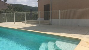 Una piscina con borde de azulejos, zona vallada y edificio de fachada color beige.