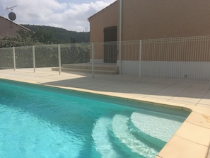 A swimming pool with a tiled edge, a fenced area, and a building with a beige exterior.