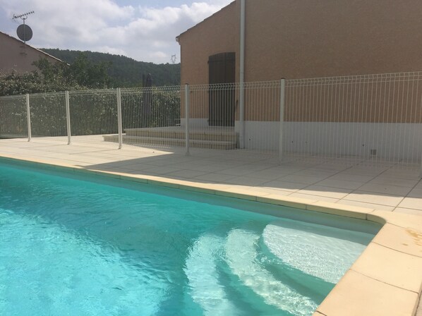 A swimming pool with a tiled edge, a fenced area, and a building with a beige exterior.