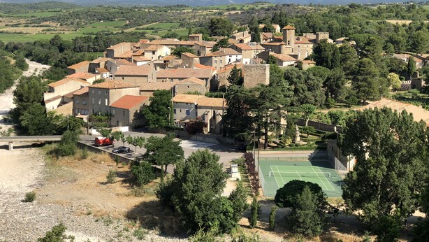 Un pueblo histórico con edificios de piedra, una torre central y una cancha de tenis.
