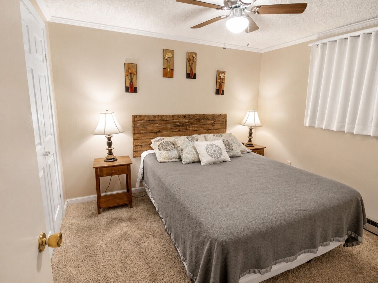 A bedroom with a bed, two bedside tables with lamps, a ceiling fan, and artwork on the wall.
