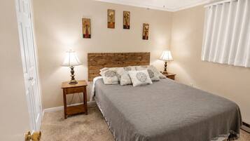 A bedroom with a bed, two bedside tables with lamps, a ceiling fan, and artwork on the wall.
