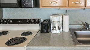 Een kitchenette met een kookplaat, broodrooster, koffiezetapparaat en een spoelbak.