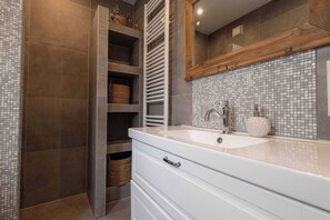 A modern bathroom with a white vanity, a tiled backsplash, and a wooden shelf unit.