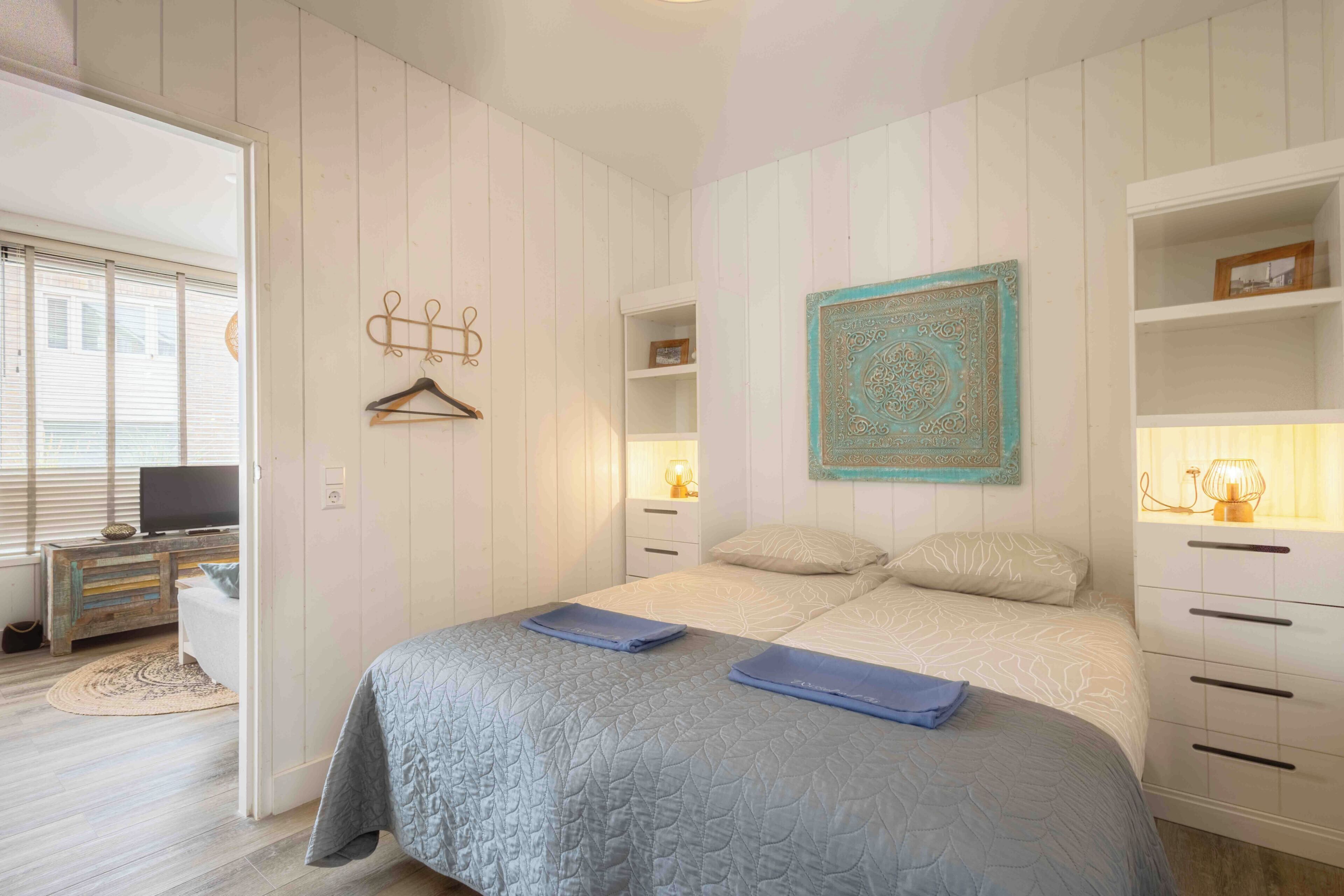 Une chambre à coucher comprenant un lit, des tables de chevet, une lampe suspendue et un élément décoratif fixé au mur.