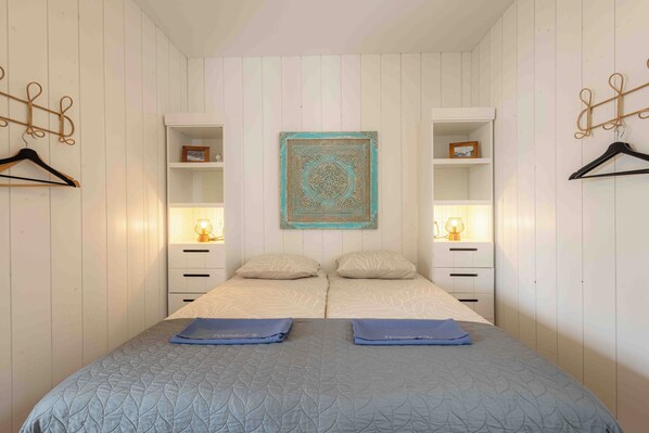 A bedroom with two beds, a decorative wall hanging, bedside lamps, and a wardrobe with hanging space. - Top location! Next to lighthouse, beach 50m EBB (Egmond aan Zee)