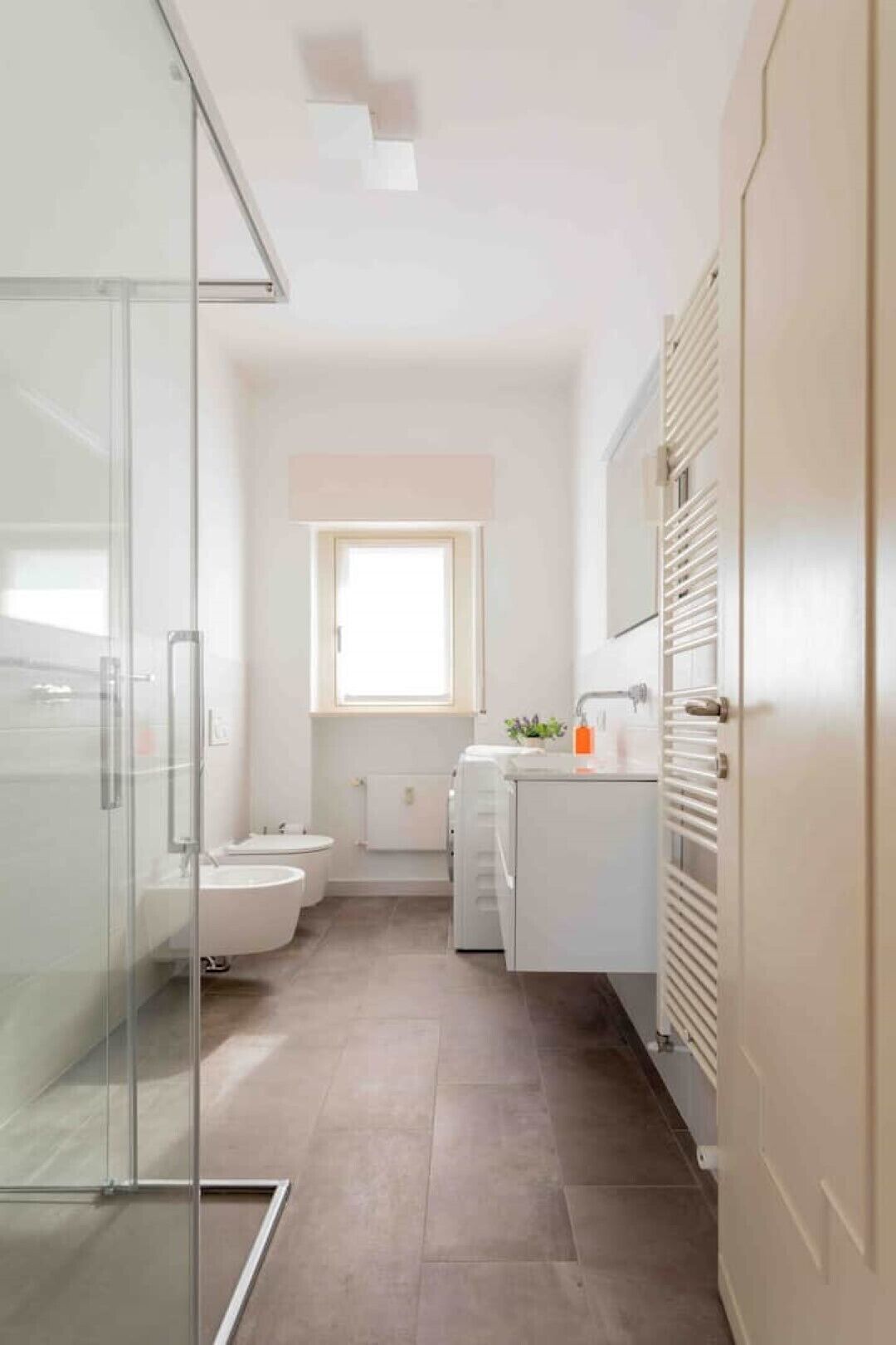 A modern bathroom with a glass shower enclosure, a toilet, a sink, and a window providing natural light.