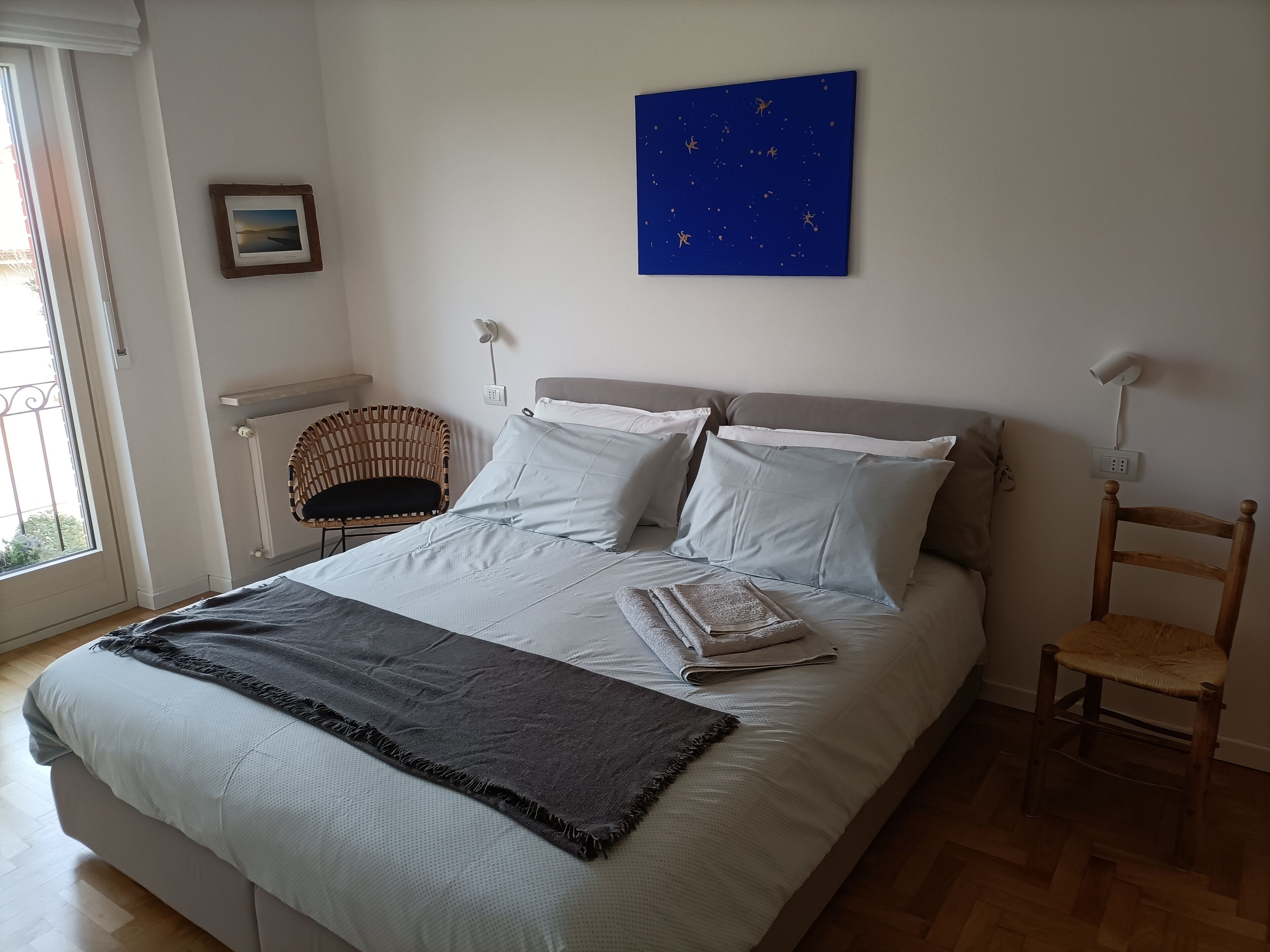 A bedroom with a bed, two chairs, a window, and a wall art piece.