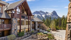 A lodge with a stone facade, wooden balconies, and a view of snow-capped mountains.