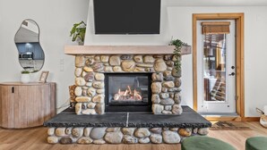 A stone fireplace with a fire, a mounted TV, and a wooden door with a window.