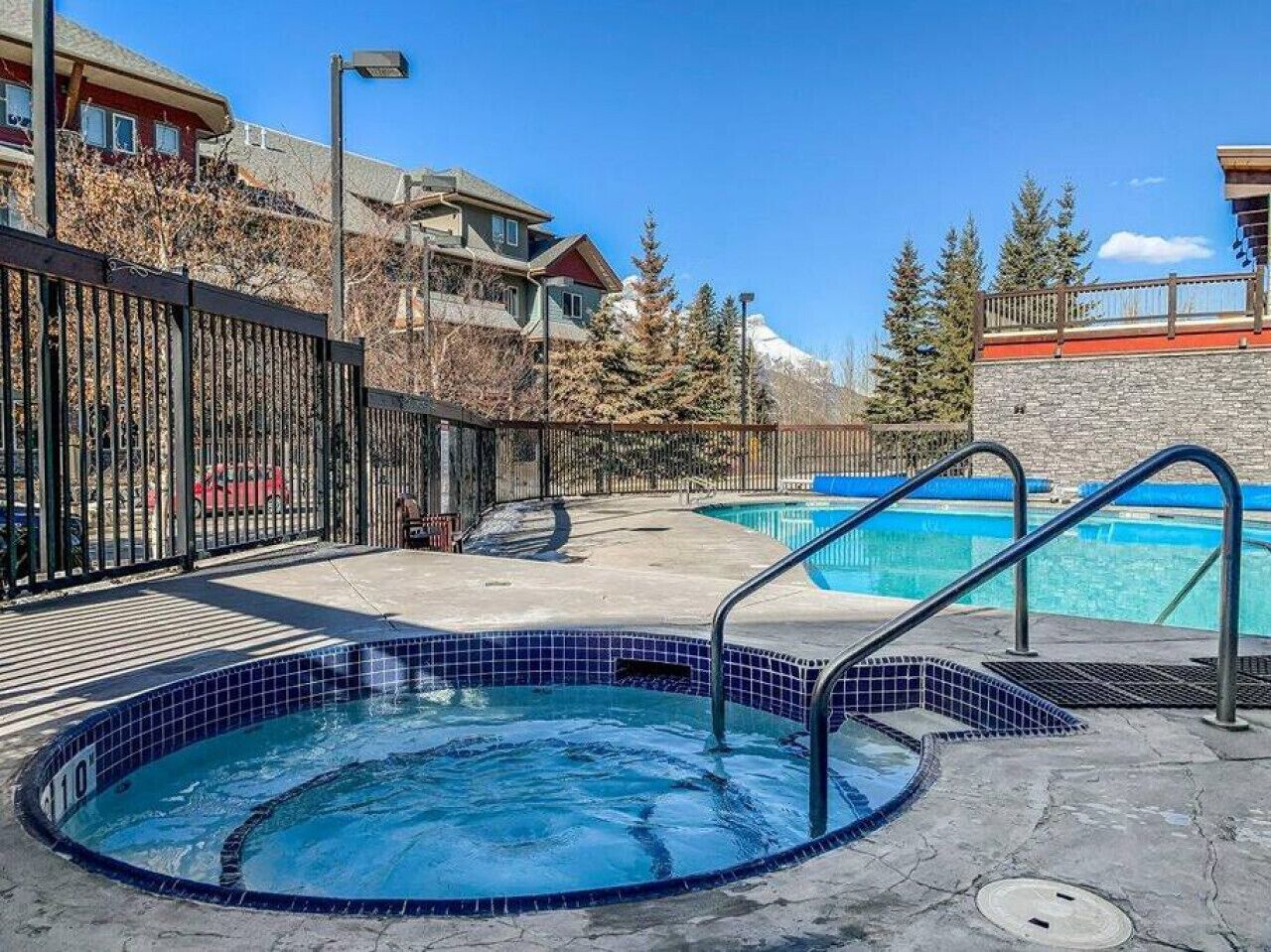 A swimming pool area with a hot tub, a wooden deck, and a view of a mountain.