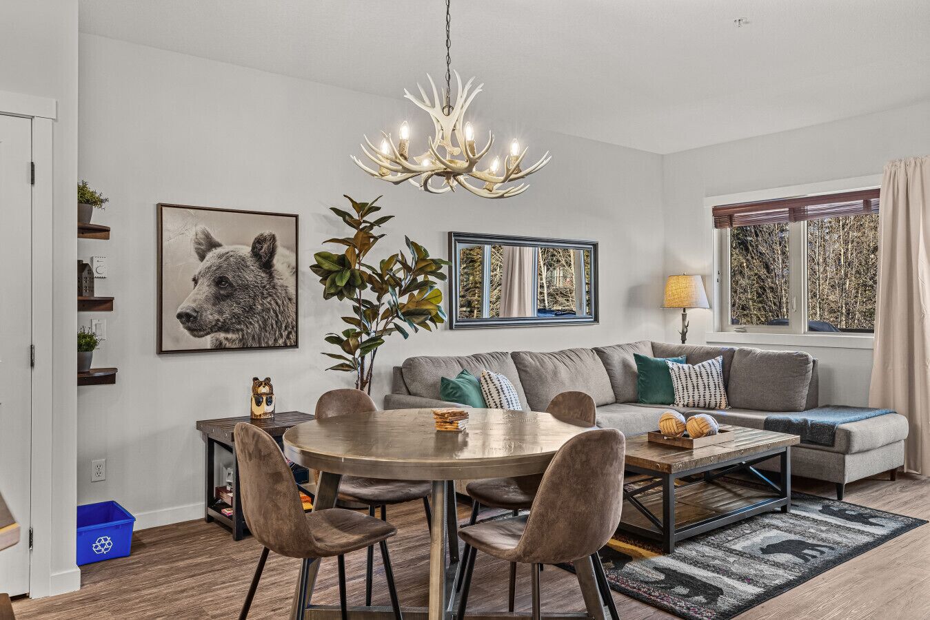 A modern living room with a round dining table, grey sofa, and a chandelier.