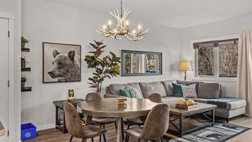 A modern living room with a round dining table, grey sofa, and a chandelier.