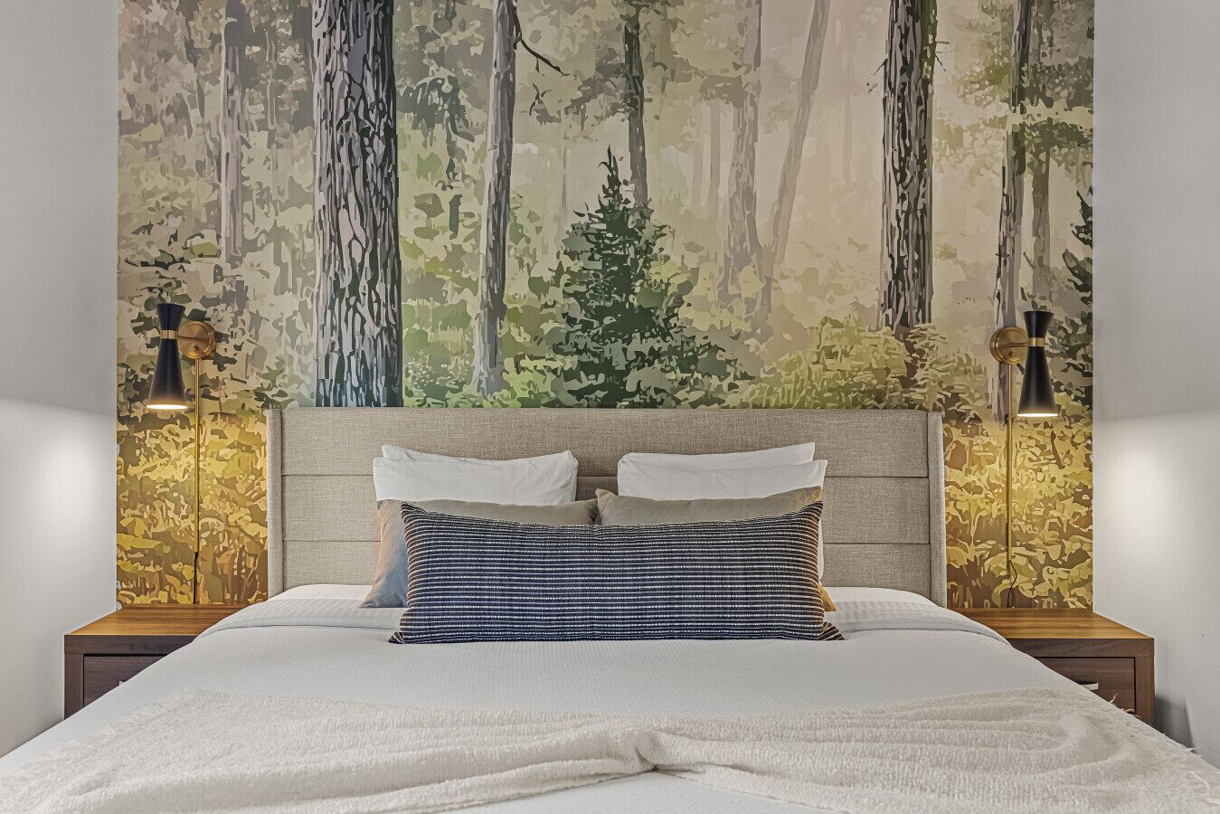 A bedroom with a bed, two nightstands, and a forest-themed wall mural.