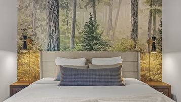 A bedroom with a bed, two nightstands, and a forest-themed wall mural.