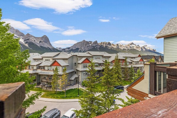 A residential area with modern houses, a central driveway, and a mountain backdrop. - 323 - 109 Montane Rd · Cozy Penthouse ~ Heated Pool/3 Hot tubs/Gym (Canmore)
