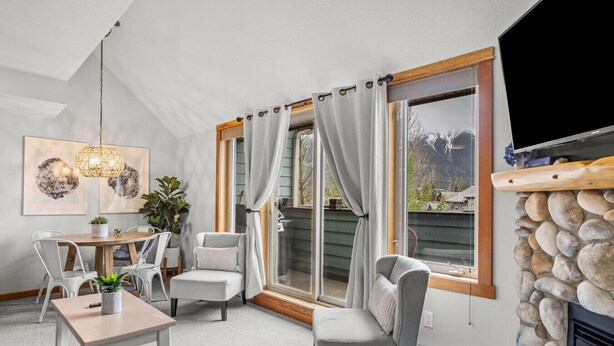 Een gezellige woonkamer met een open haard, een eethoek met een tafel en stoelen, en een groot raam met gordijnen.
