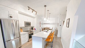 Une cuisine moderne avec des meubles blancs, des appareils en acier inoxydable et un îlot central doté de tabourets de bar.