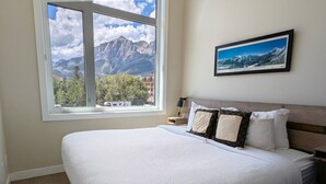 Une chambre avec un grand lit, une fenêtre donnant sur la montagne, une table de chevet et un tableau encadré au mur.