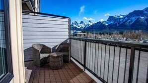 Un balcon agrémenté de meubles en osier, une vue sur des montagnes enneigées et un parking en arrière-plan.