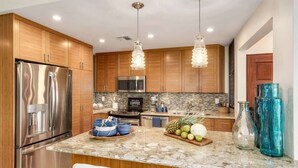 Una cocina moderna con armarios de madera, electrodomésticos de acero inoxidable, encimera de granito e iluminación colgante.