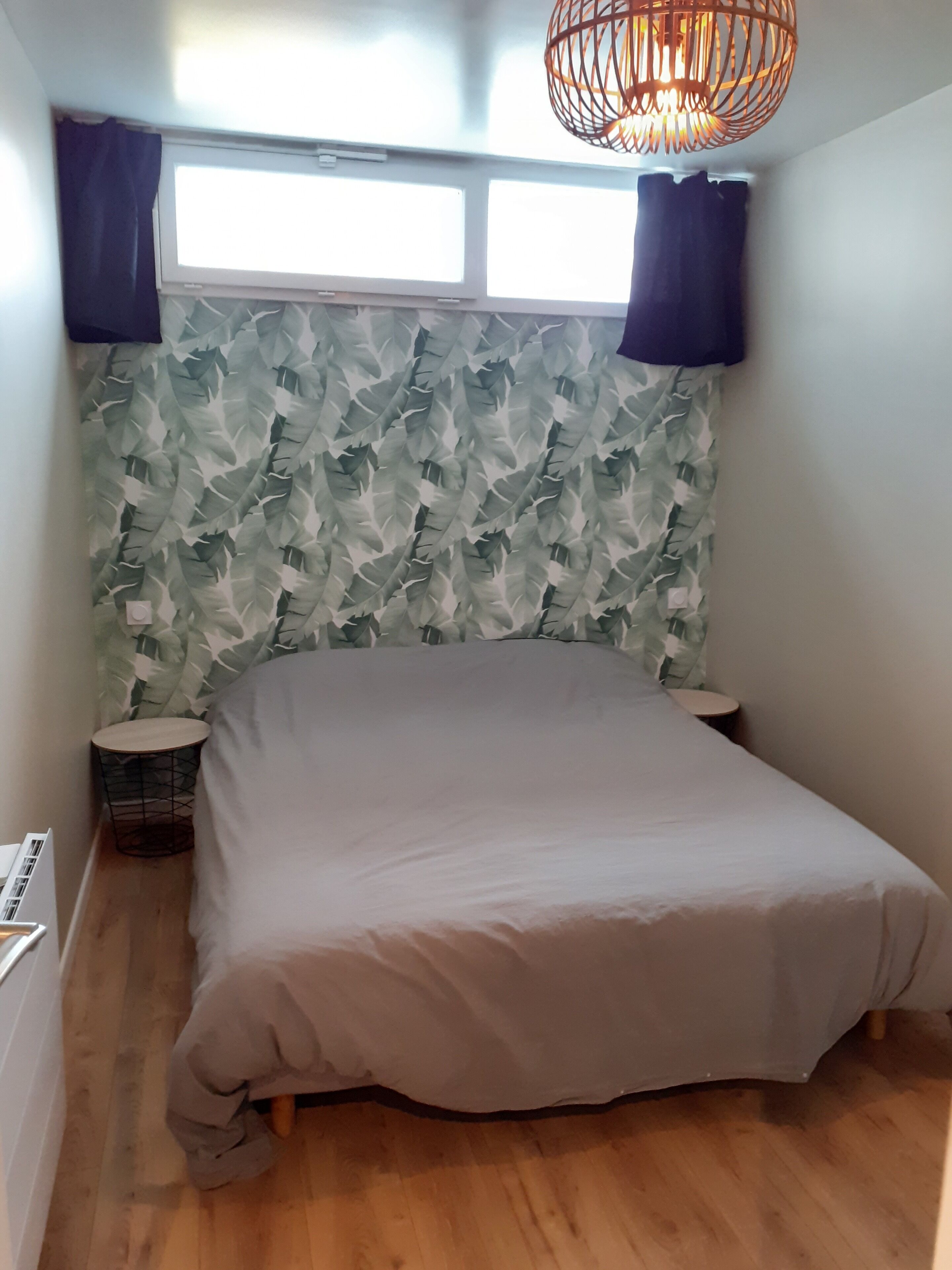 A bedroom with a bed, two nightstands, a round side table, a window with curtains, and a hanging light fixture.