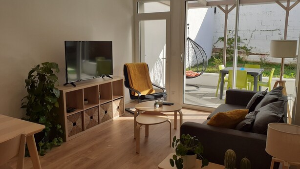 A modern living room with a flat-screen TV, a sofa, a chair, and a small table. - KALEE Garden apartment (Lanester)