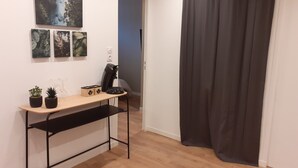 A room with a wooden desk, two potted plants, a coffee machine, and a black chair. There are three framed pictures on the wall and a black curtain on the door. - KALEE Garden apartment (Lanester)