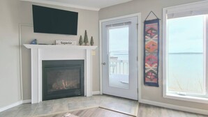 Quarto com lareira, porta para uma varanda e grande janela com vista para a água.