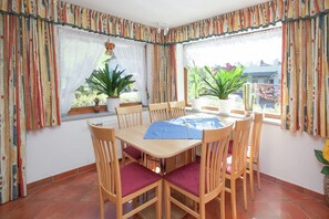 Un coin repas avec une table et des chaises en bois, des plantes en pot et des rideaux colorés.