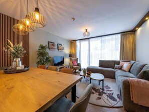 A modern living room with a wooden dining table, a sofa, and a TV.