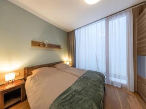 Et hotelværelse med en seng, sengeborde med lamper, en træsenggavl, et vindue med gardiner og en hylde med pynt.