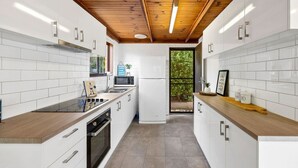 A modern kitchen with white cabinetry, a wooden ceiling, and a view through a glass door to the outdoors.