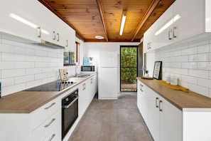 A modern kitchen with white cabinetry, a wooden ceiling, and a view through a glass door to the outdoors.