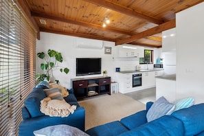 A modern living room with a blue sofa, a flat-screen TV, and a wooden ceiling.