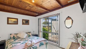 A bedroom with a bed, a nightstand, a mirror, and a view through a sliding glass door.