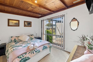 A bedroom with a bed, a nightstand, a mirror, and a view through a sliding glass door.