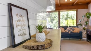 A framed inspirational quote on a wall, a wooden table with a potted plant, and a sofa in a modern living room with large windows.