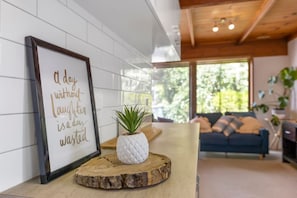 A framed inspirational quote on a wall, a wooden table with a potted plant, and a sofa in a modern living room with large windows.