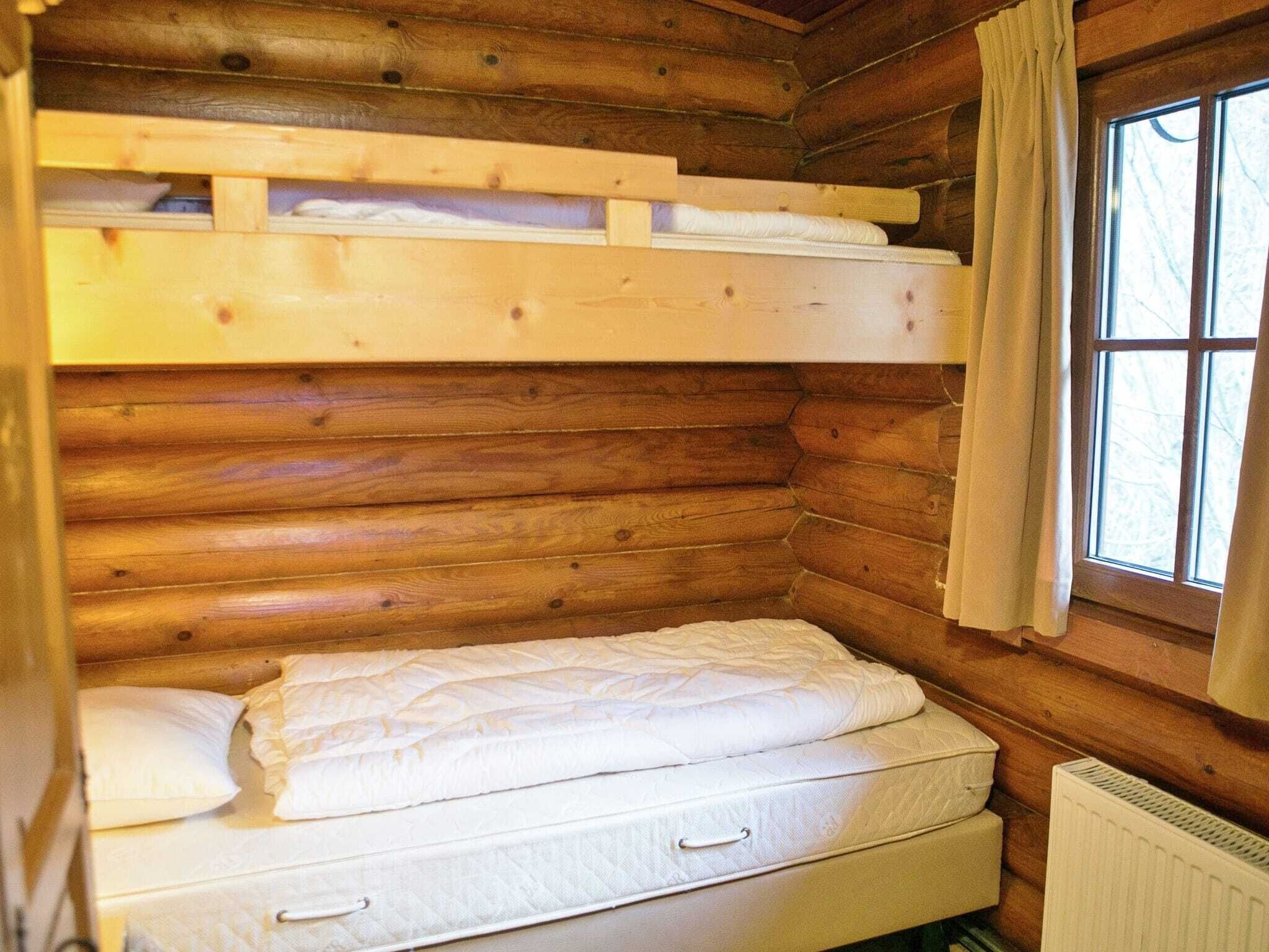 A wooden cabin room with a bunk bed, a window with curtains, and a radiator.