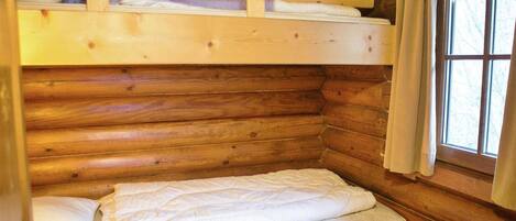 A wooden cabin room with a bunk bed, a window with curtains, and a radiator.