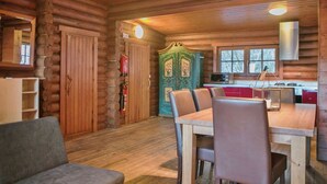 L’intérieur d’une cabane en rondins comprend un coin repas, une cuisine avec des meubles rouges et une porte verte ornée de motifs floraux.