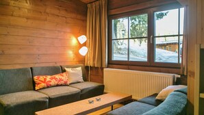 Une pièce chaleureuse avec un décor intérieur en bois, un canapé, une table et une fenêtre donnant sur un paysage enneigé.