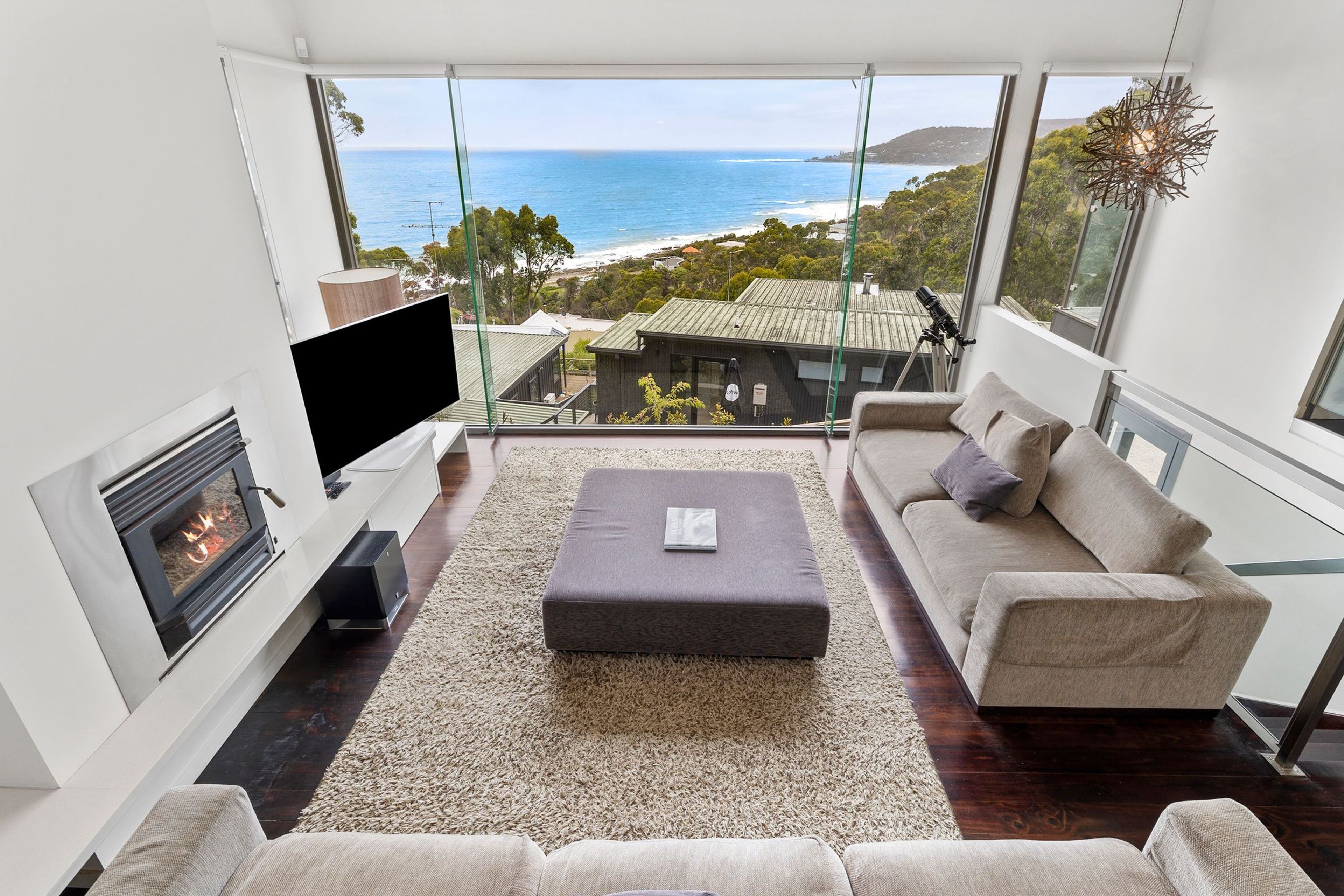 Una sala de estar moderna con un televisor grande, asientos cómodos, una chimenea y vistas al océano.